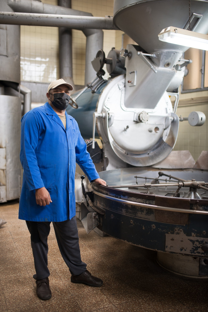 man wearing mask standing next to coffee roasting machine man wearing mask standing next to coffee roasting machine