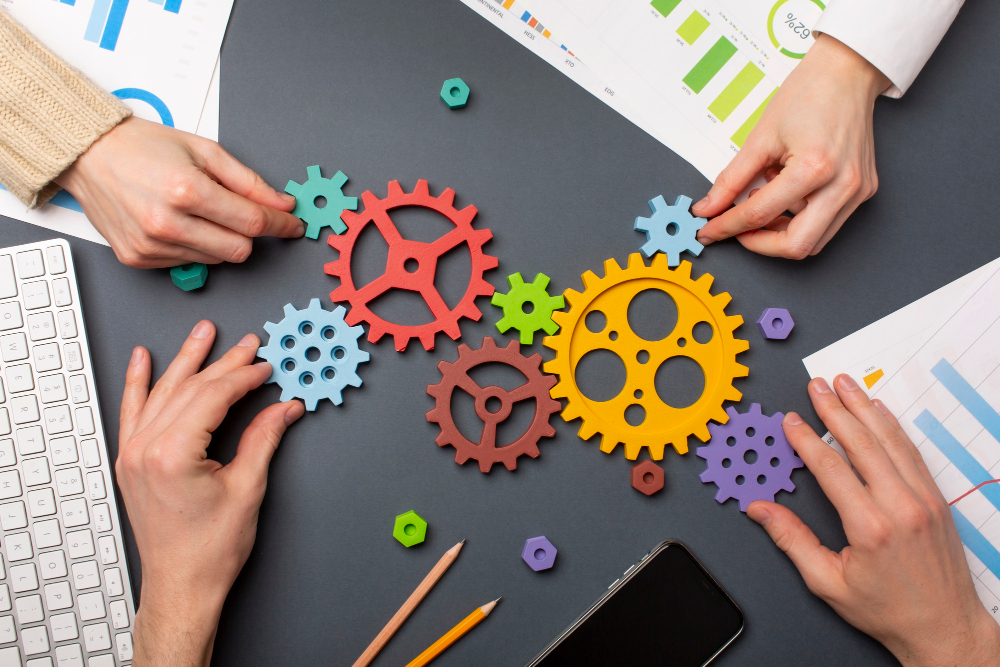 cogs on a desk with paperwork and several helping hands cogs on a desk with paperwork and several helping hands