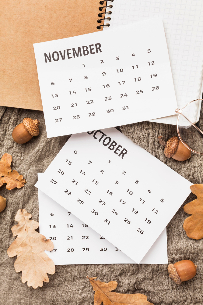 three pages of monthly calendars, scattered, with autumnal leaves and acorns in the background three pages of monthly calendars, scattered, with autumnal leaves and acorns in the background