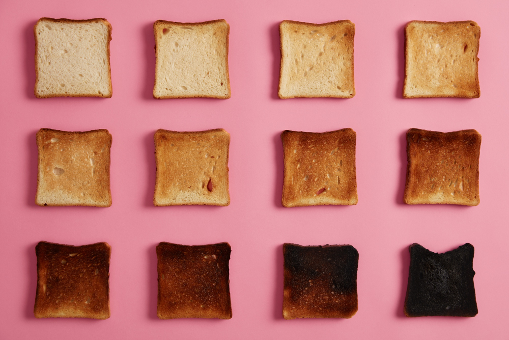 Isolated overhead shot of bread toasts in different stages of roasting against pink background. Last slice is completely burnt. From unroasted to charred. Isolated overhead shot of bread toasts in different stages of roasting against pink background. Last slice is completely burnt. From unroasted to charred.