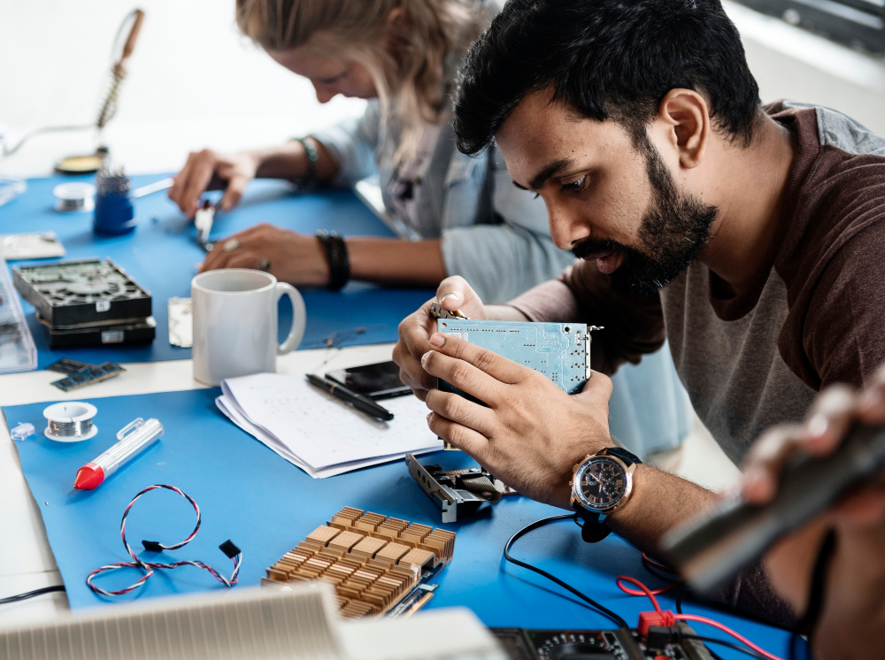 two technicians (one woman, one man) working on electronics parts two technicians (one woman, one man) working on electronics parts