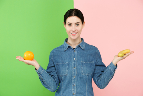 woman holding orange and banana in either hand to compare them woman holding orange and banana in either hand to compare them